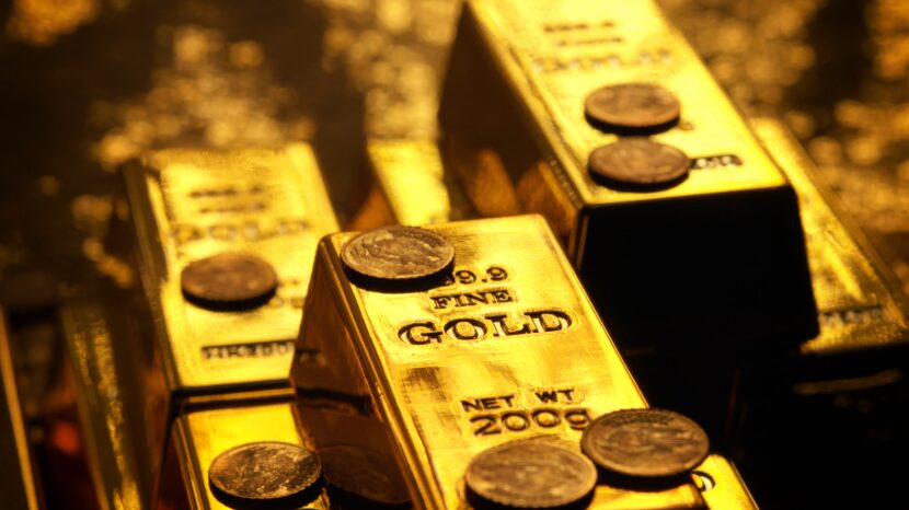 Gold bars in a pile with gold coins scattered around the bars